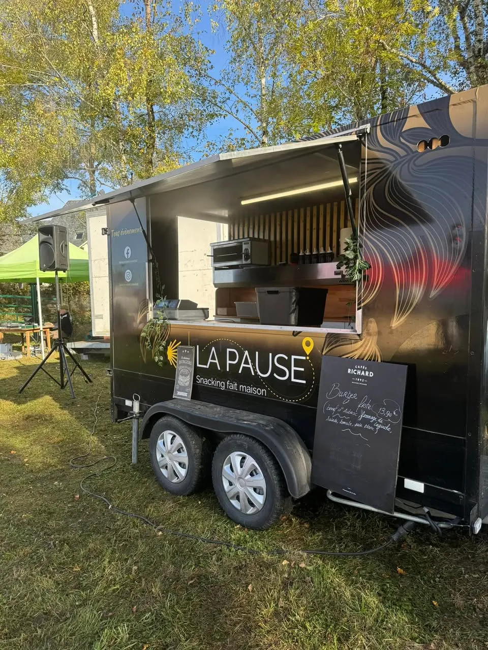 Le food truck noir aux feuillages dorés, ouvert lors d'une fête en plein air sous les arbres