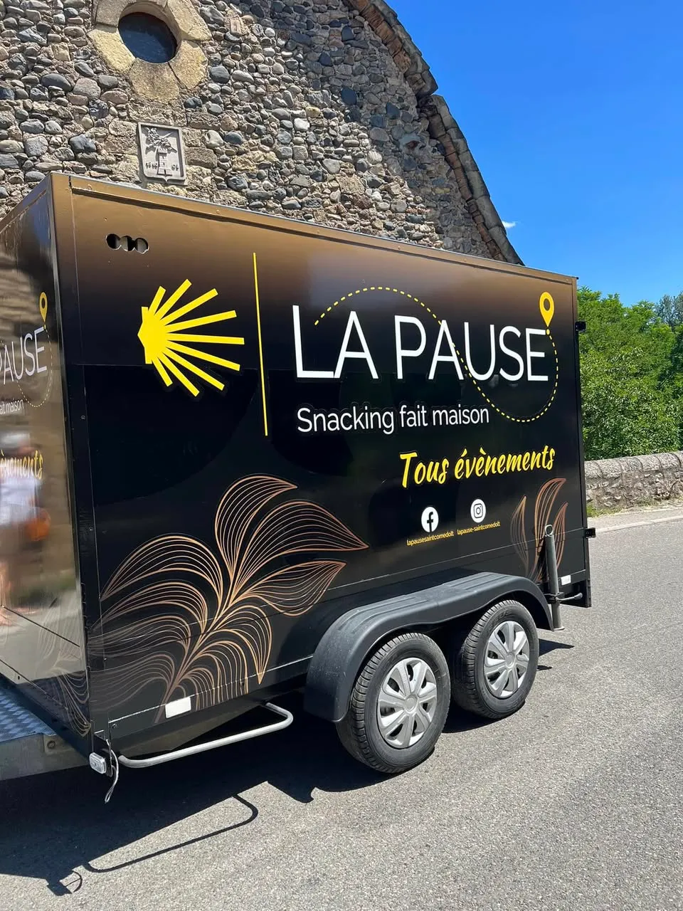 Le food truck noir aux feuillages dorés, garé devant une église en pierre